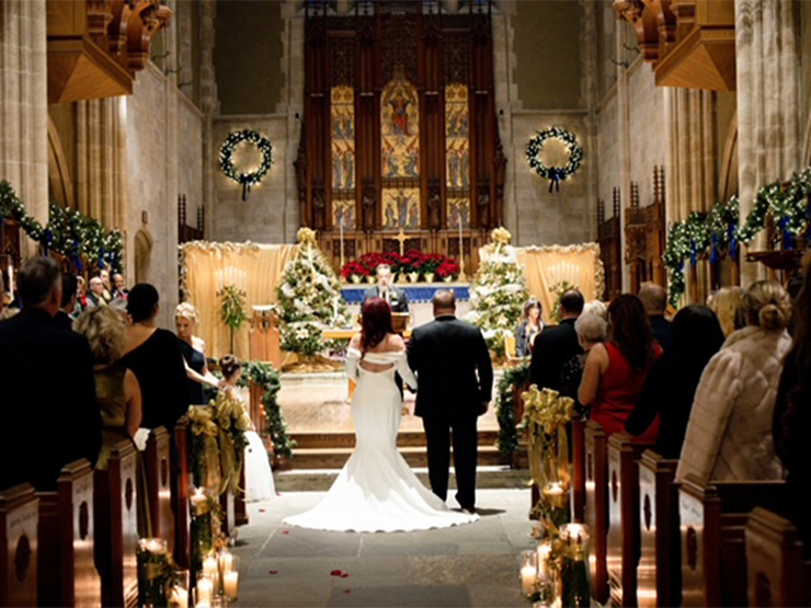A bride and groom stand at the alter of a historic chapel decorated in flowers and candles for a wedding ceremony..