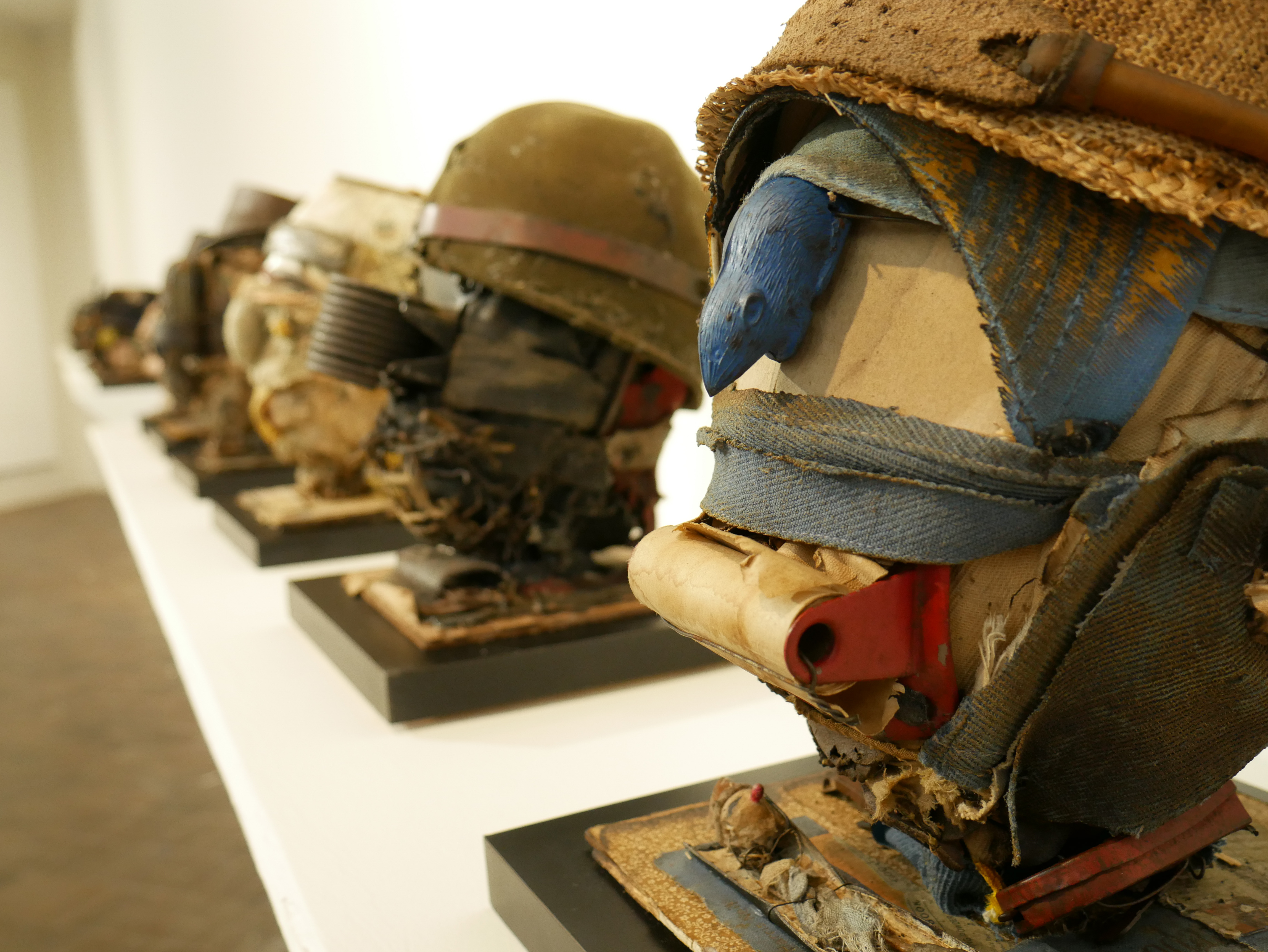 A row of busts constructed from found materials are displayed in a museum gallery space.