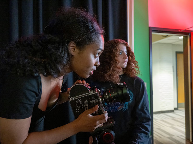 A pair of young adults work together on a video camera in a production room.