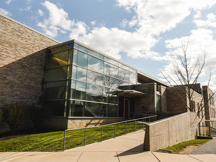 The entry way to South Hall, a residence hall with a large glass foyer, sits under sunny blue skies.