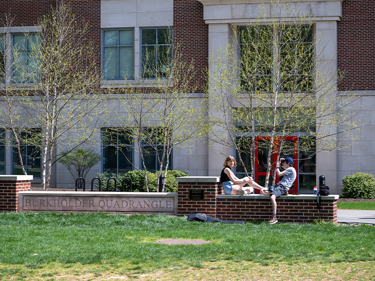A pair of student, one photographing the other, hang out on a sunny day on Muhlenberg's Burkholder Quad.