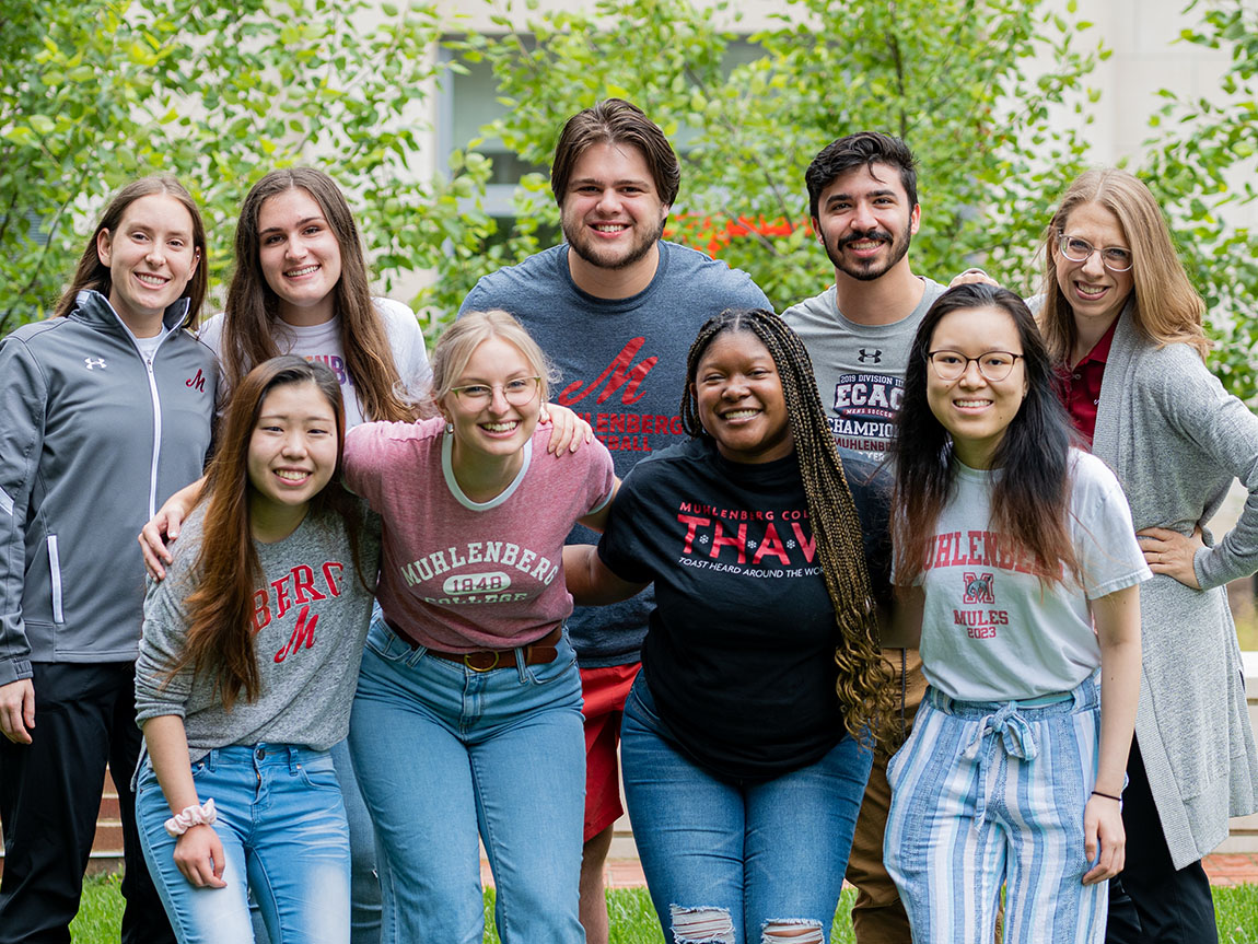 A group of college students and faculty stand outside smiling and posing for a group photo