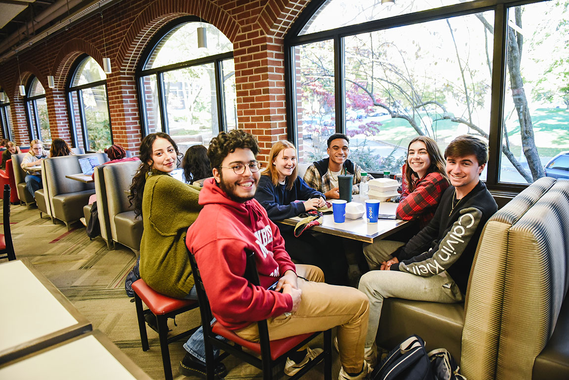 Six smiling college students gather around a table
