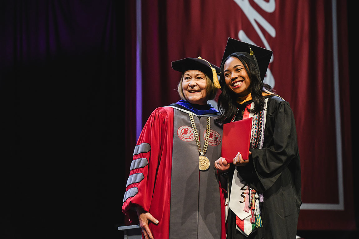 A college president and a student pose in regalia with the student's diploma