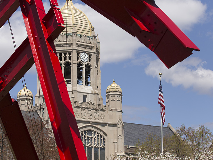 View of Haas clocktower on a sunny day with red steel sculpture in foreground.
