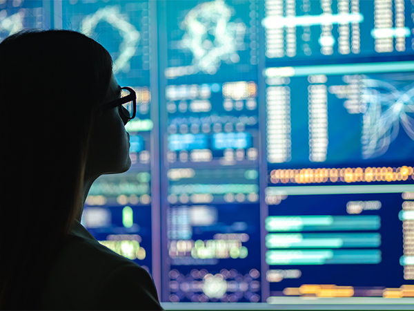 The silhouette of a woman looks at a large board of electronic data and maps.