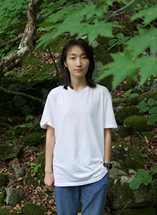 Portrait photo of Advanced Counseling Trainee, Jinghui (Cheng) Jin, standing posed in outdoor wooded setting with foliage.