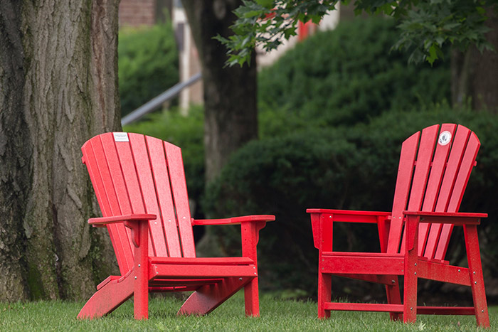 Two red adirondack chairs sit next to one another outside.