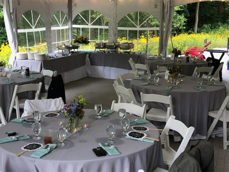 Table settings are arranged under an outdoor canopy with yellow flowers blooming in the distance.