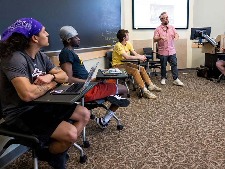 Students look on as an instructor speaks to a classroom in a playwriting class.