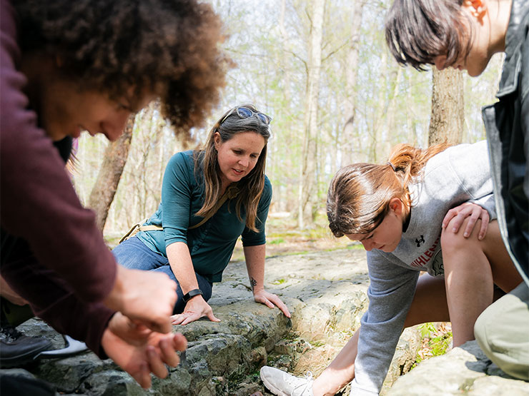 A college instructor and a group of students lean over a streambed at Ringing Rocks County Park.