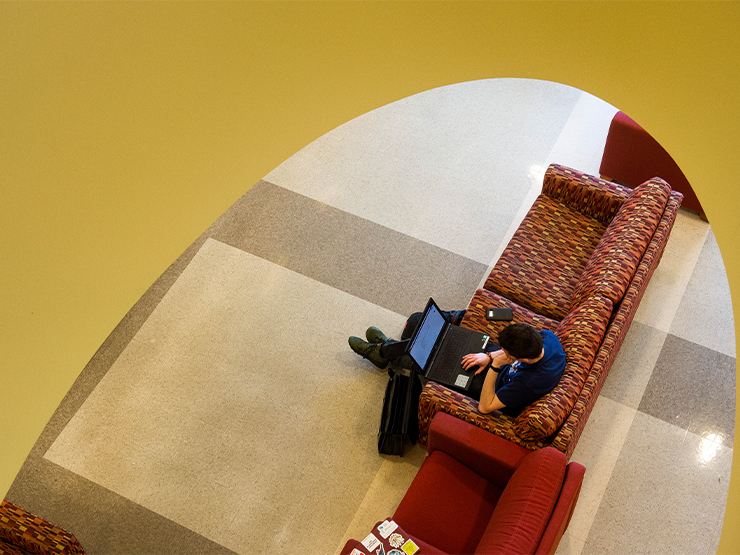 Viewed from above, a student is sitting on a couch with an open laptop.