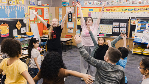 Two college students in a second grade classroom lead the kids in a dance