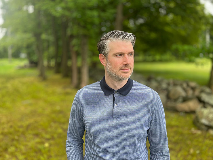 A man in a striped shirt looks off into the distance while walking outdoors.