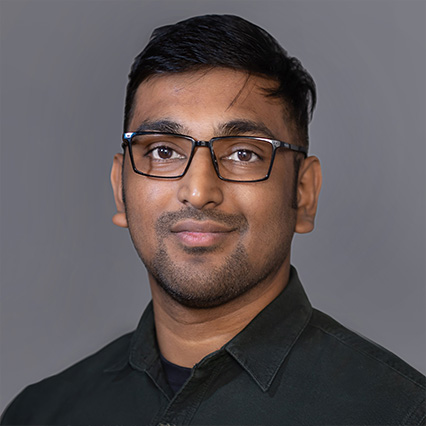 Profile image of faculty member Proyash Podder standing against grey background backdrop.