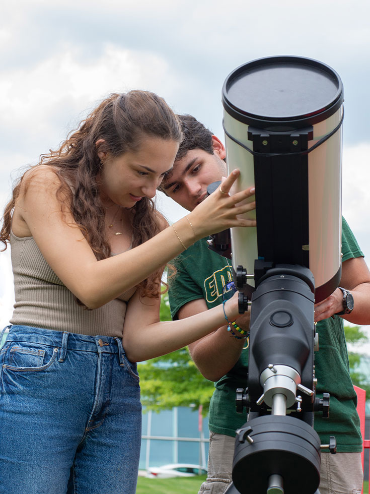 A pair of students work on a telescope outdoors.