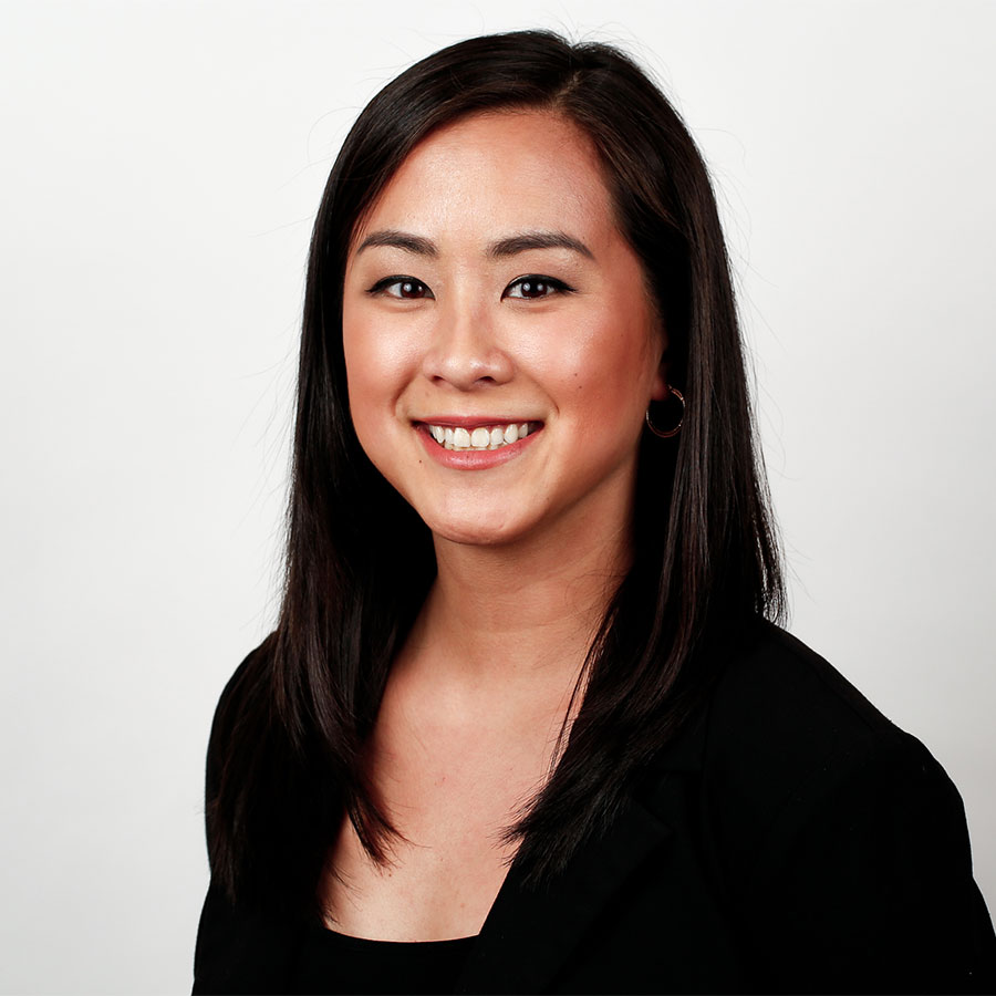 A headshot of a media professional with long dark hair, wearing a dark blouse and blazer.