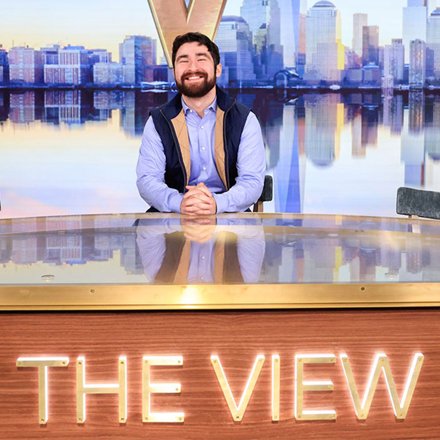 Julian David Torres smiles while seated behind the desk on the set of The View.