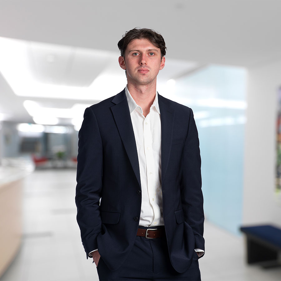 A young lawyer in a blazer and white button down shirt poses for a headshot.