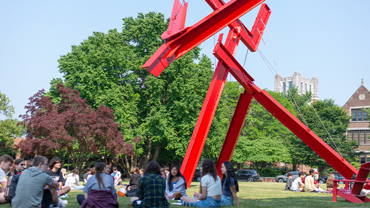 Groups of students sit on the College lawn beneath the large, red modern sculpture Victors Lament.