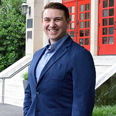 A man in a blue suit smiles while standing outdoors on the campus of Muhlenberg College.