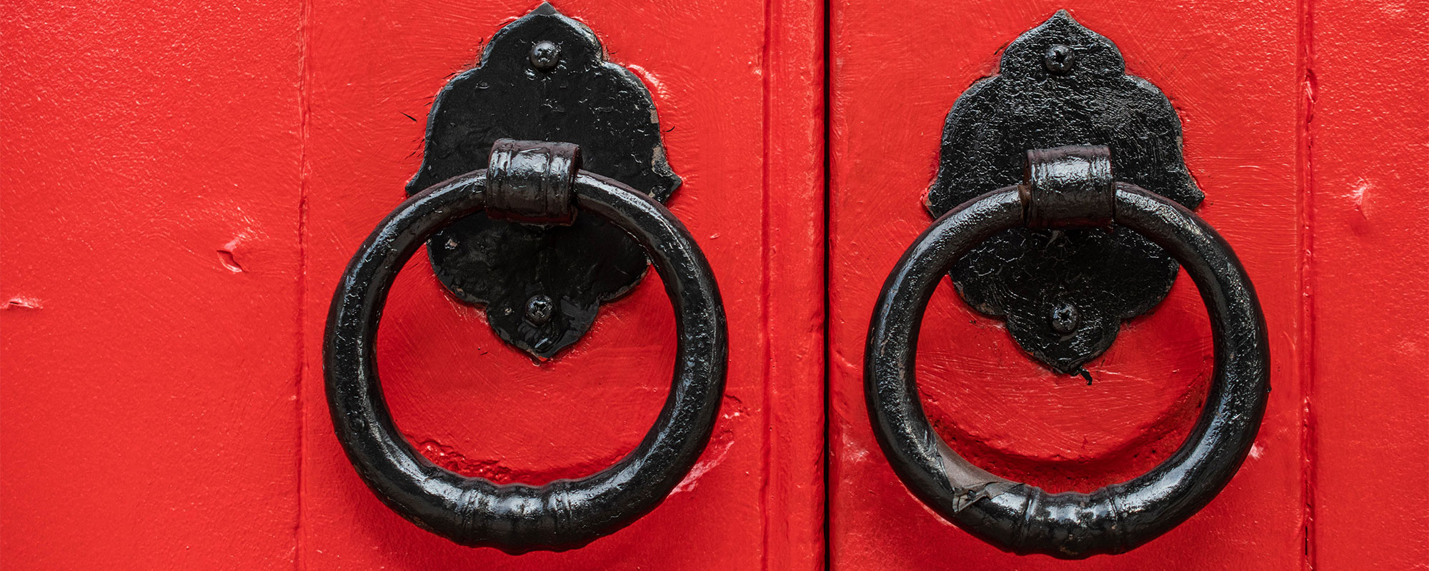 A close up of a pair of painted red doors and ornate black metal door handles.