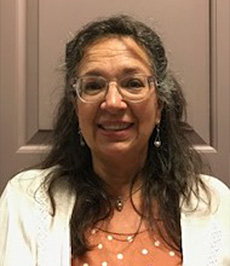 Portrait of Administrative Assistant, Susan Lawrence wearing a white sweater and glasses in indoor setting.