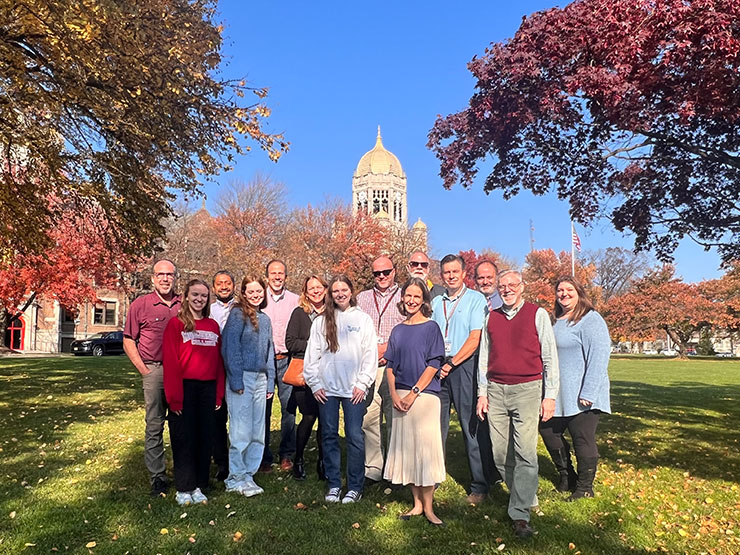 A group of several faculty and staff members at Muhlenberg College smile and pose on the College green with the Haas clocktower in the distance.