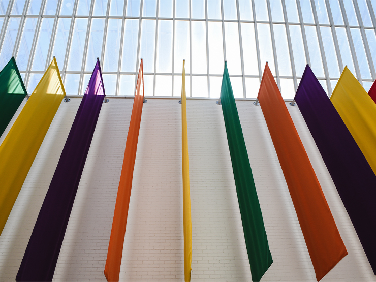 A row of large, colorful flags hang off a white brick wall in the Baker Center for the Arts.