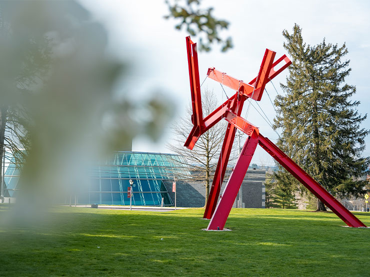 The blur of a white tree blossom partially obscure the view of Victor's Lament, a large red modern sculpture.