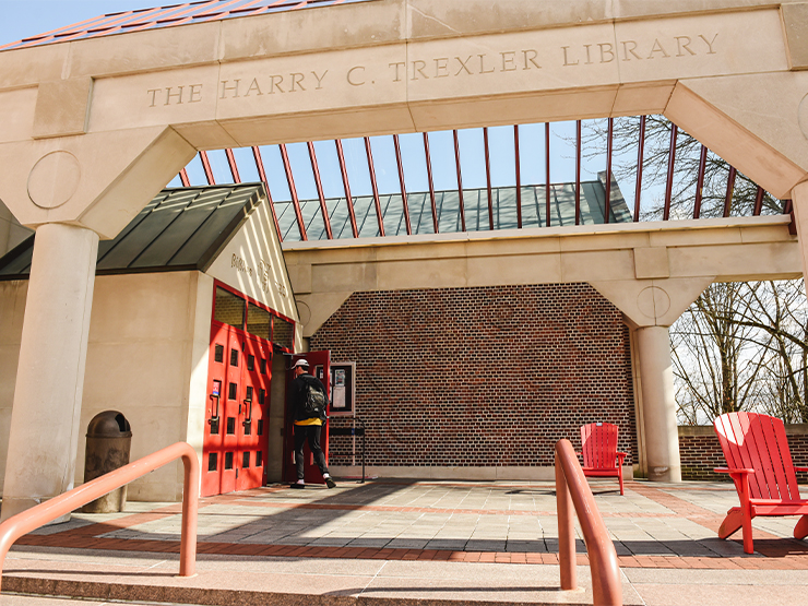 A student walks into the red door entrance of the Trexler Library.