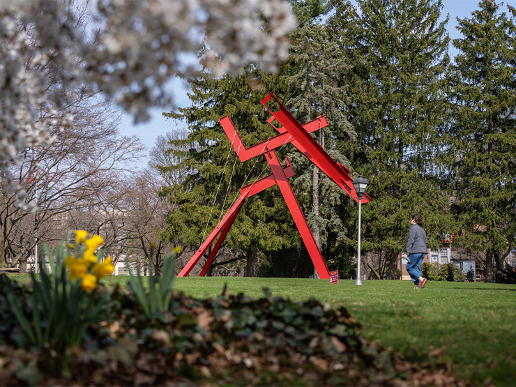 The red modern sculpture Victors Lament framed by newly budding trees and spring flowers.