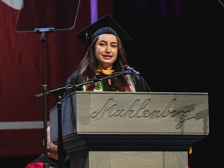 College senior Teigan Brown speaks from behind a podium during a commencement ceremony.