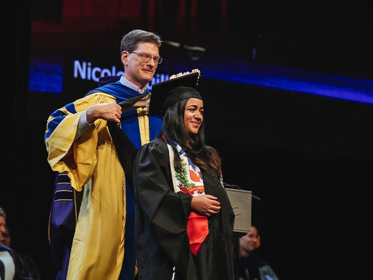 A Muhlenberg dean drapes an academic hood over the shoulders of a new master's degree graduate.