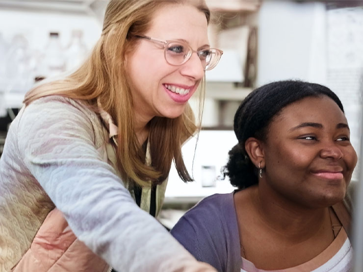 An instructor leans over the shoulder of a student in a lab.