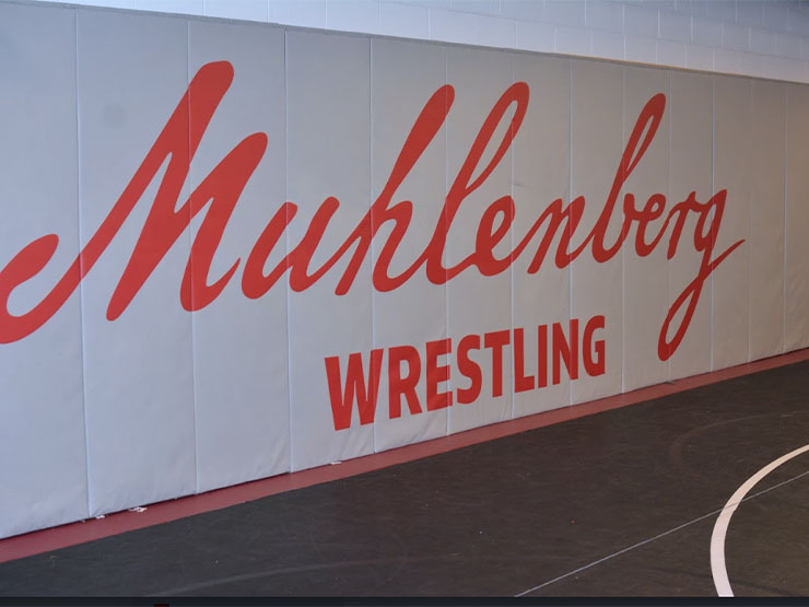 Red script on a grey padded wall of a gymnasium reads 