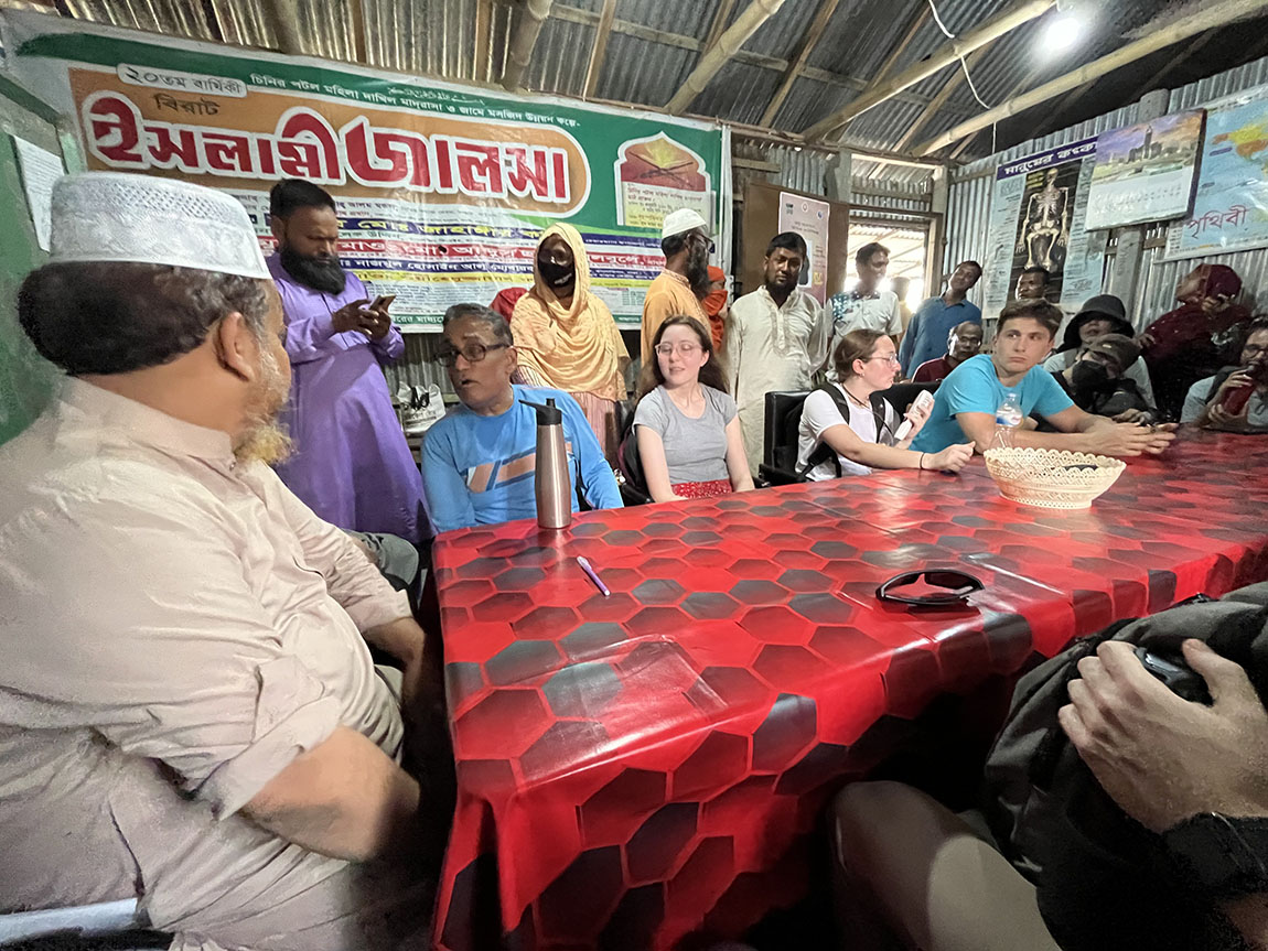 A group of people, some from the United States and some from Bangladesh, sit around a table with a red tablecloth and talk