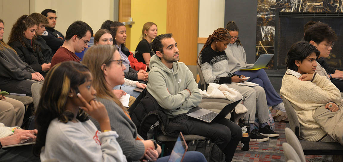 A seated crowd of students and faculty listens to a panel discussion