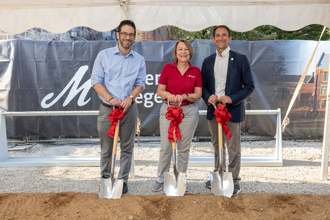 Three people smile for a photo while holding shovels with red bows on them