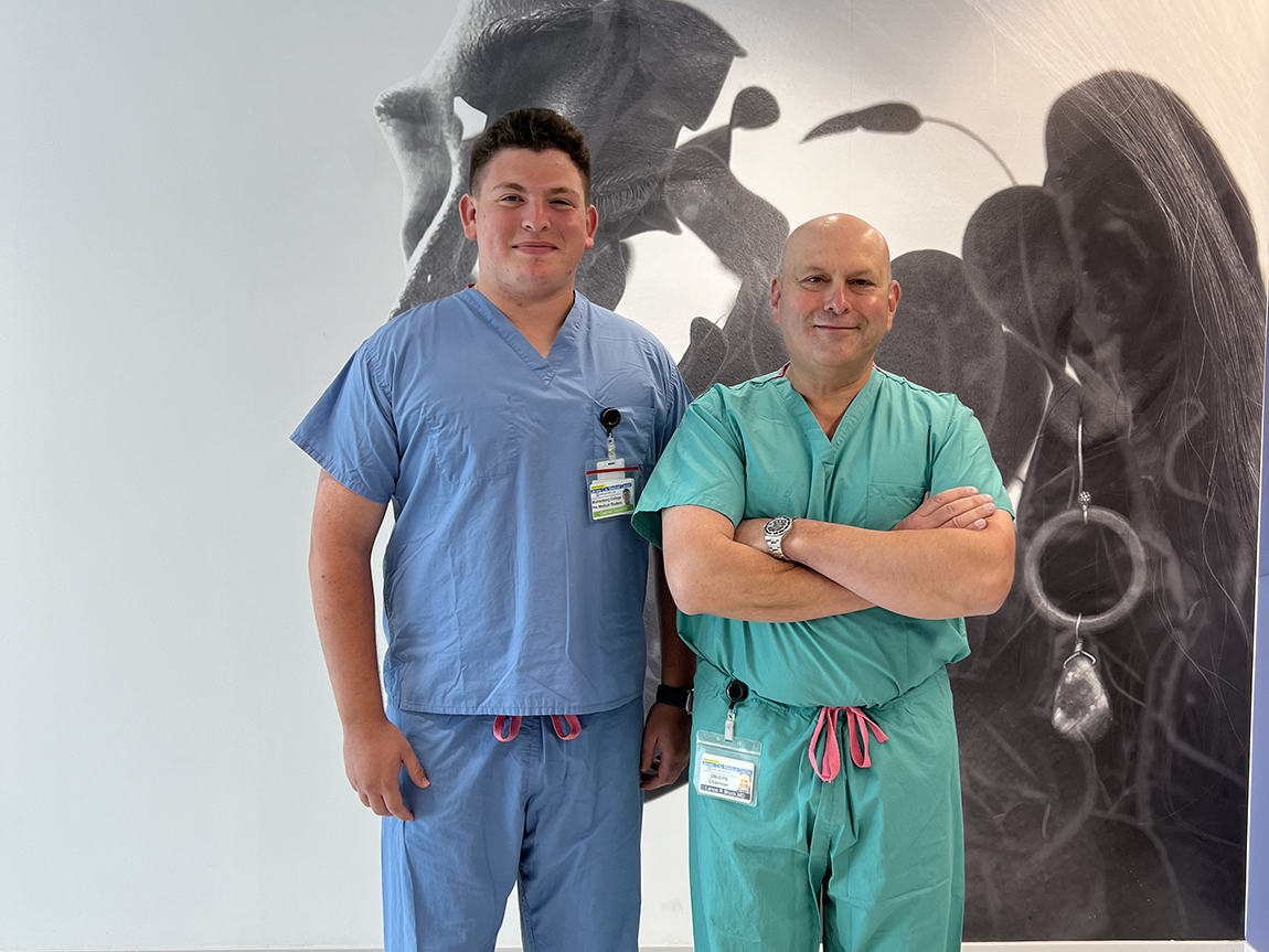 A college student in blue scrubs stands next to a doctor in green scrubs