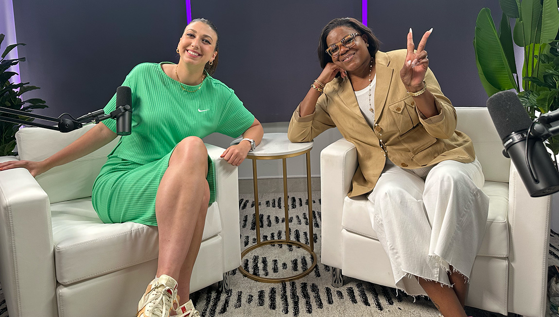 A young person in a green dress smiles next to an older person in a brown blazer who is giving a peace sign.