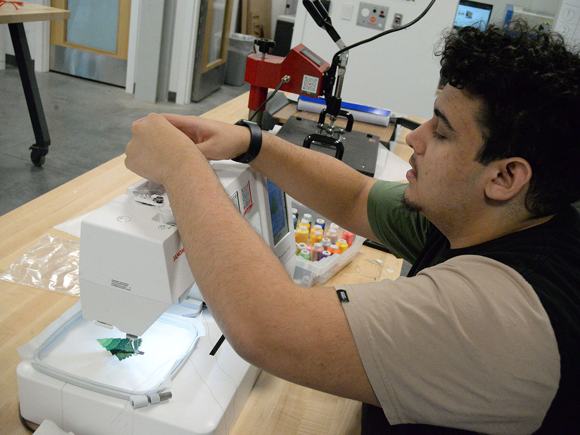 A student uses a sewing machine to embroider a Christmas tree