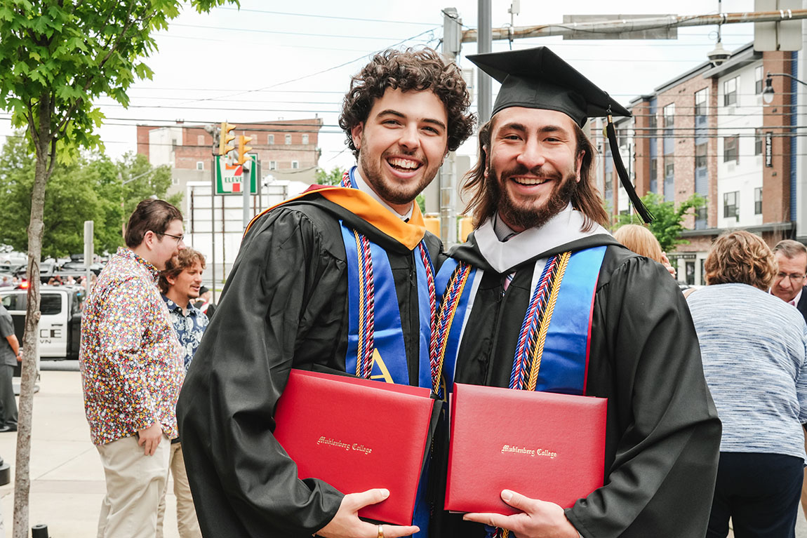 Two college graduates smile for a photo after commencement
