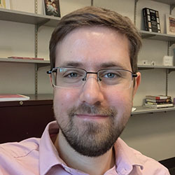 A college professor with brown hair and beard and glasses on photographed in his office