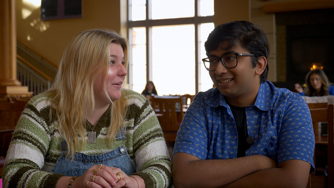 Two college students sit for an interview in a dining hall