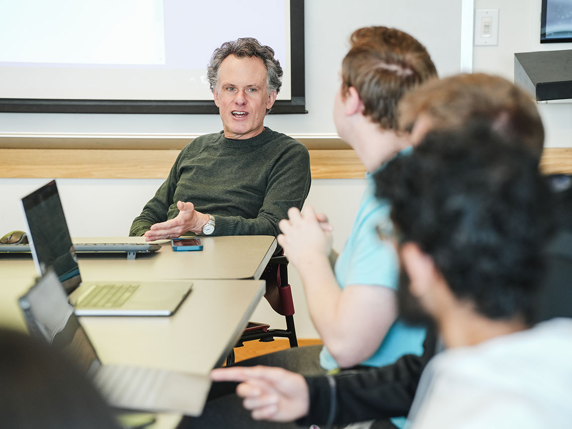 A college professor in a green sweater converses with students during class