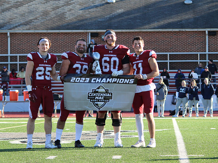 A group of football players in Muhlenberg College gear holding a banner that reads 