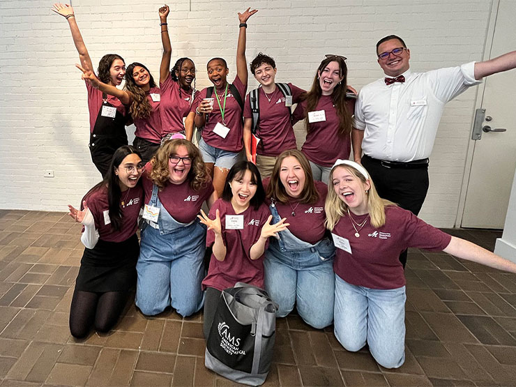 A group of young adults pose playfully for a photo alongside a member of college staff.