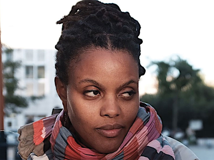 A college professor wearing a colorful scarf, looks off-camera.