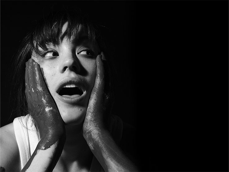 An person holds painted hands to face with a surprised expression in stylized black and white.